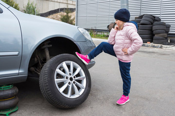  A small child standing in front of his broken car looking at the wheel.