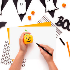 Woman drawing smiling face on Halloween paper pumpkin