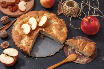 Apple Pie Charlotte on a black wooden table with red apples in iron form.