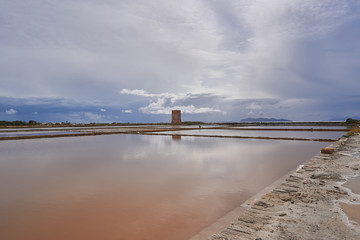 Torre Nubia near Salina Culcasi of Paceco. Saltpans in traditional salt production in Trapani in Sicily during the sunset with cloudy sky and calm sea. Riserva naturale integrale Saline di Trapani.