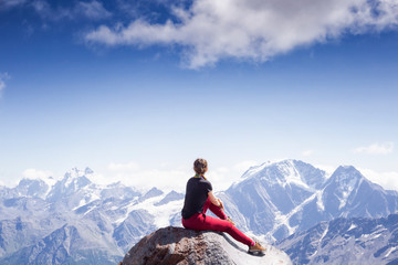 a young active girl sits on the edge of a rock, look at the Caucasus mountains. girl on backdrop of...
