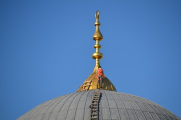 Fototapeta na wymiar A worker in an orange jacket on the dome of a mosque cleans the Spire.