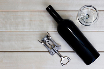 top view on a corkscrew, a bottle of red wine and a glass on a wooden table with free space for text