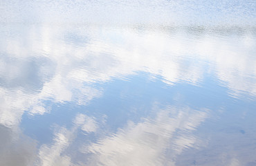 Bright white and dark clouds are reflected in lake water. Light ripples from wind on surface of pond. Place for text, copy space. Selective focus image.