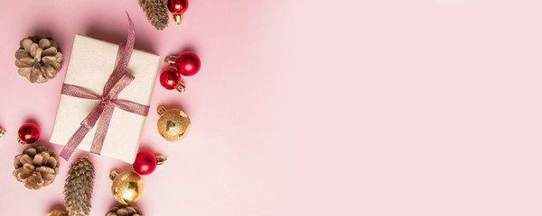 Christmas gift box with red ribbon, pine cone, gold and red balls on a pink background.