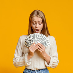 Shocked young girl holding fan of dollar banknotes