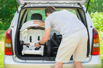 Young man loading parts of baby carriage in opened car trunk. Preparing to become parent for future...