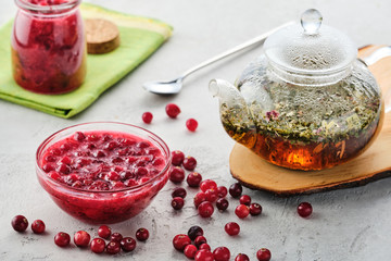 Cranberry jam in a glass bowl and teapot on a white background.