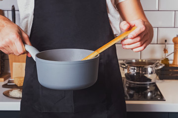 Man's hands close-up holding a saucepan and stirring with wooden spoon.