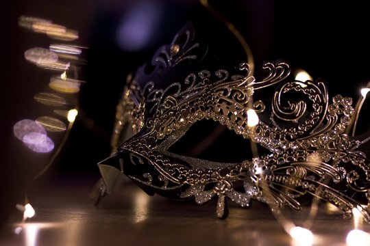 A portrait of a mysterious mask on a wooden table surrounded by lights. It is perfect to hide someones identity on a venetian masked ball.