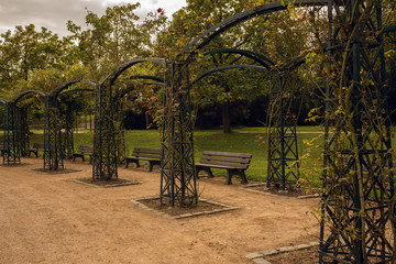 Dirty gravel road with  benches and arches in a park in autumn with yellow, green and red trees