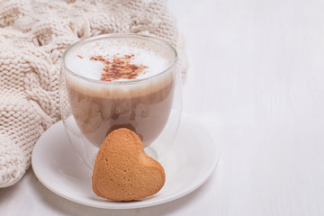 A cup of latte sprinkled with cinnamon and a heart shape biscuit