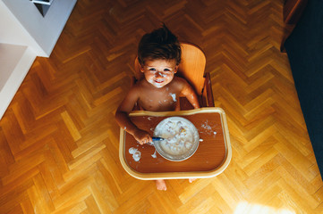 Little boy eating breakfast at home, sitting in high chair, from above