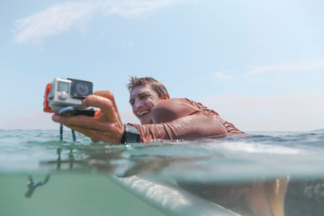 Surfer with action camera lying on surfboard