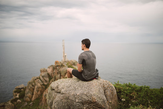 Trail runner sitting on a rock in coastal landscape, Ferrol, Spain