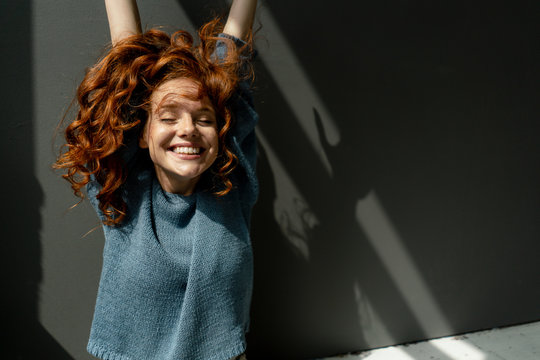 Portrait of happy redheaded woman with eyes closed raising hands