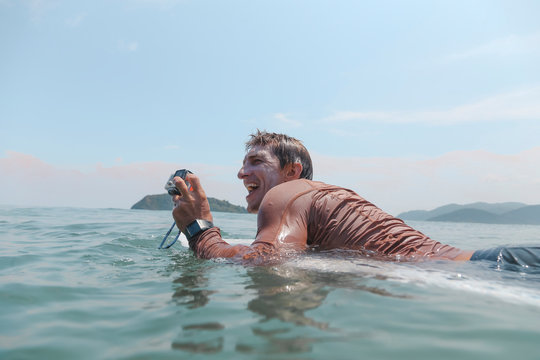 Surfer with action camera lying on surfboard