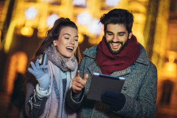 Young couple in the city centre with holiday's brights in background. Couple browsing digital tablet. They are using credit card for online shopping.