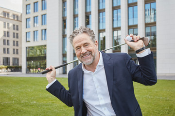Portrait of happy mature, businessman with golf club in the city