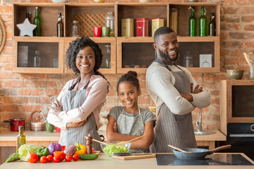 Condifent family in aprons posing over kitchen background