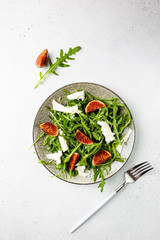 Delicious salad with figs, arugula and goat cheese on white plate, top view, copy space