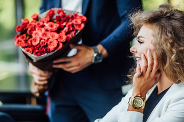 Focus at big red bouquet of roses, blonde woman looking at gift, celebrating time.