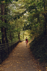 A girl walking on a path with fallen leaves on a sunny fall day in a park, lifestyle image,