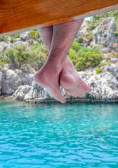 Bare feet hanging from wooden pier over sea water. Holiday vacation by the sea.