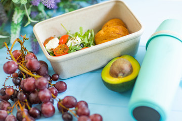 Close up of plastic container with healthy school lunch, thermos and grape on table.