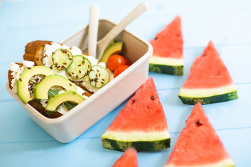 Fruits in lunch box with corn flakes, yogurt, fresh apricots, plums and grapes, sanwish and watermelon on table. Vegeterian eat.