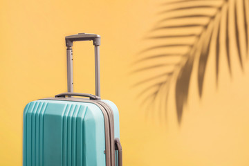Suitcase for travel on the yellow background with palm leaf shadow.