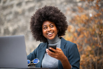happy business woman sitting outside with laptop and mobile phone in hand