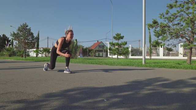 Girl sprinter in a black top and leggings is training in a run park. Sprinter woman stands in pose for start and starts running.