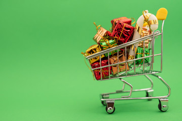 New Year's gifts and toys in supermarket trolley on green background. Christmas shopping concept