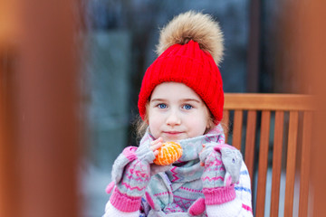 little girl in a red hat eats mandarin