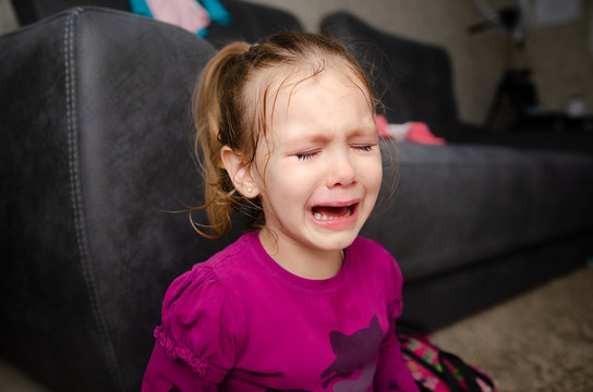 Little girl sitting on the floor, she is upset and crying. The child is crying sitting on the floor in the room.
