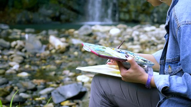 close-up. Woman artist . hands on nature against the backdrop of a waterfall. paint in the palette