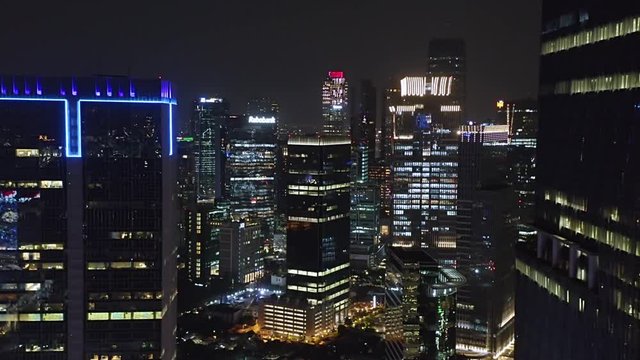 JAKARTA, Indonesia - October 03, 2019: Exotic aerial landscape of modern skyscrapers in financial district with night lights. Shot in 4k resolution from a drone flying from left to right