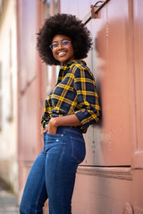 Fototapeta na wymiar smiling young african american woman with afro hair leaning against wall
