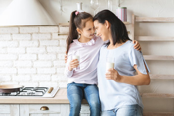 Mother and daughter drinking milk in kitchen and touching foreheads