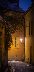 Narrow street of an old city during the night in winter. Romatic scene with snow-covered path and shining lamp.
