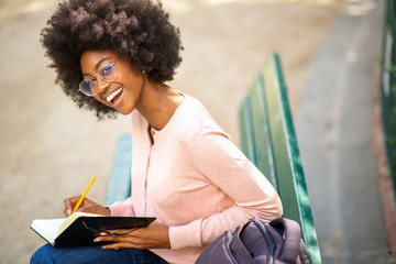 young smiling african american woman with glasses writing in book