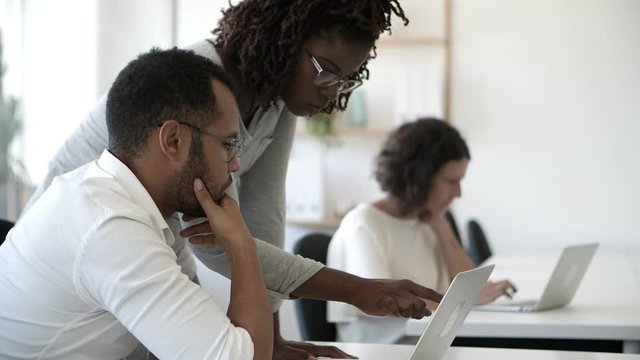 Concentrated African American woman pointing at laptop. Focused colleagues working with laptop at office. Teamwork concept