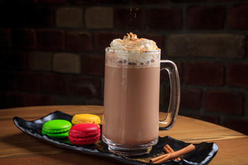 Tall glass with coffee with cream, cinnamon and multi-colored macaroons in a black plate on a wooden background