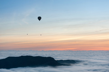 A group of hot air balloons flies over a sea of clouds in the region of La Garrotxa, in Girona (Spain) at dawn.
