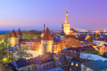 Fototapeta premium Historical old town of Tallinn, Estonia illuminated at night, after sunset, under a beautiful clear and colorful, purple and pink dusk sky. Aerial view.