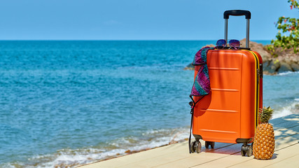 Turquoise sea, orange suitcase, sunglasses, swimsuit. Relax started.