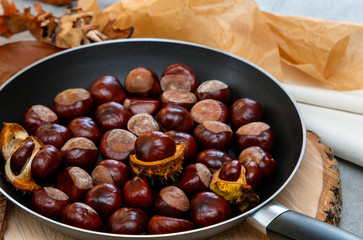fresh clean shiny chestnuts in a pan with autumn foliage and paper parcels