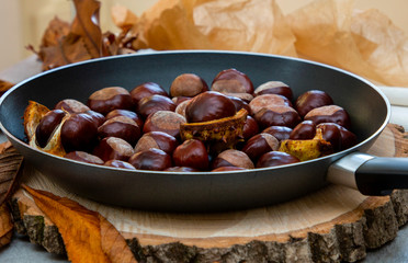 fresh clean shiny chestnuts in a pan with autumn foliage and paper parcels