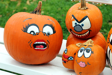 Orange pumpkins with funny drawn ghost faces are on the bench as decoration for outdoor autumn holiday in the park. Funny vegetables. Harvest and halloween concept.